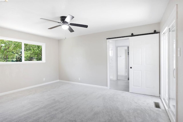 empty room with ceiling fan, a barn door, and light colored carpet