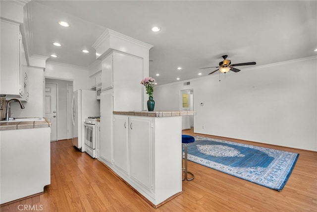 kitchen featuring a breakfast bar, light wood-type flooring, sink, white cabinets, and white appliances