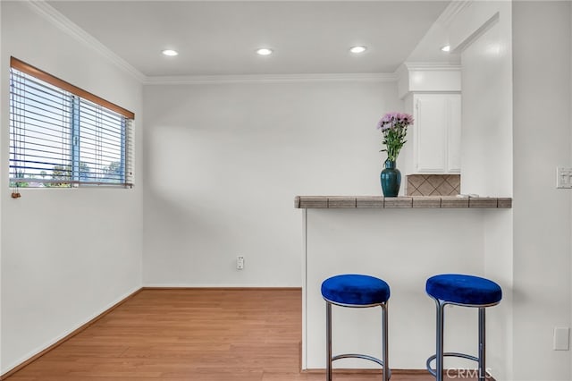 kitchen featuring white cabinets, tile countertops, a breakfast bar, light hardwood / wood-style floors, and decorative backsplash