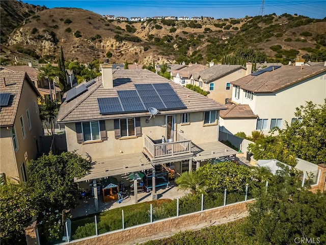 rear view of house with a chimney, a deck with mountain view, a fenced backyard, stucco siding, and solar panels