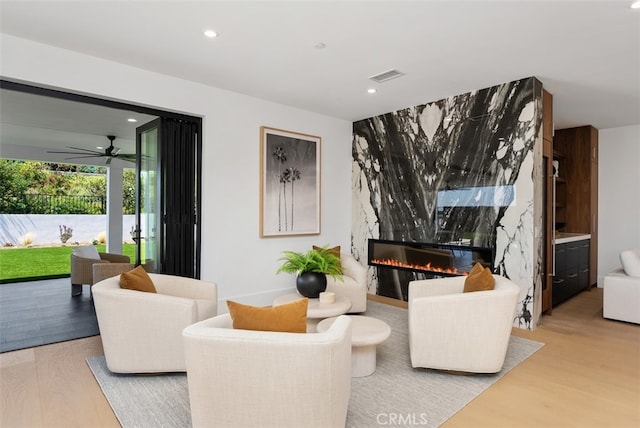 living room featuring light wood-type flooring, a premium fireplace, and ceiling fan