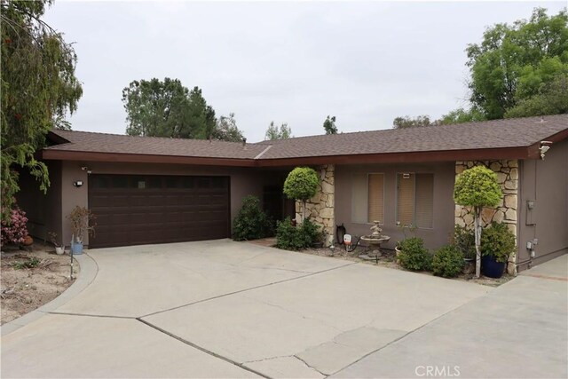ranch-style house with stone siding, concrete driveway, stucco siding, and a garage