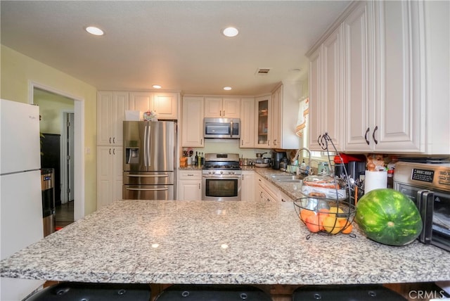 kitchen with light stone countertops, stainless steel appliances, sink, and white cabinetry