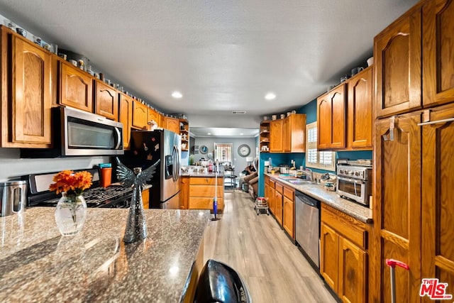 kitchen with stone counters, sink, stainless steel appliances, light hardwood / wood-style flooring, and a textured ceiling