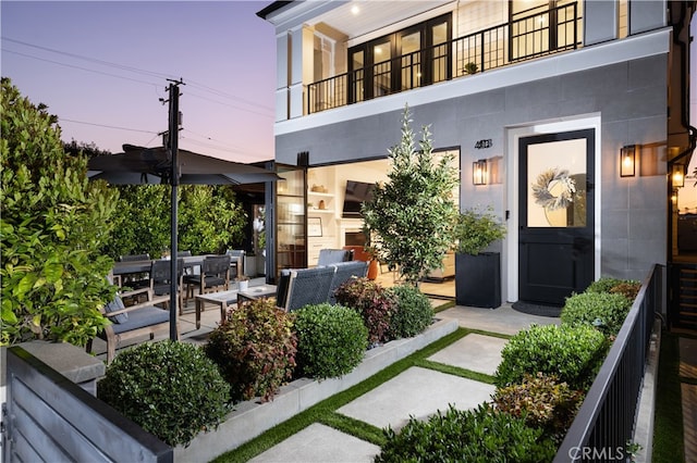 exterior entry at dusk with an outdoor hangout area, a balcony, and a patio area