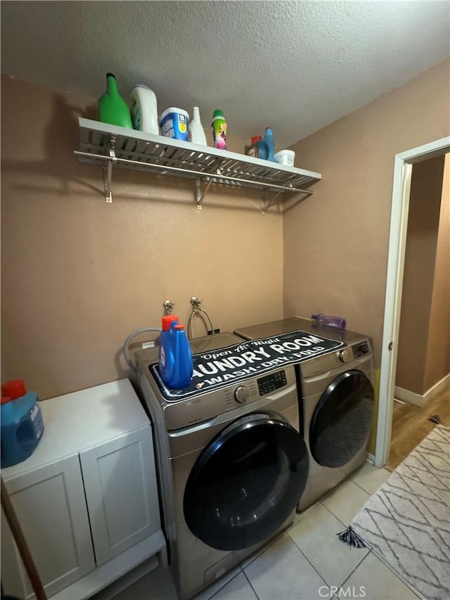 clothes washing area with cabinets, washing machine and dryer, light tile patterned floors, and a textured ceiling