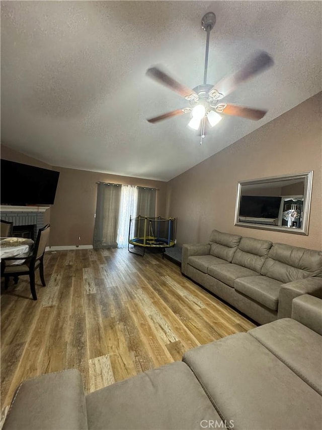 living room featuring vaulted ceiling, a fireplace, a textured ceiling, and hardwood / wood-style flooring