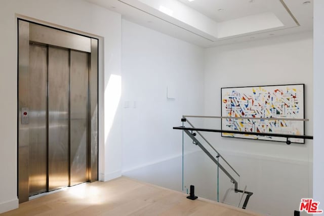 stairway with wood-type flooring, a raised ceiling, and elevator