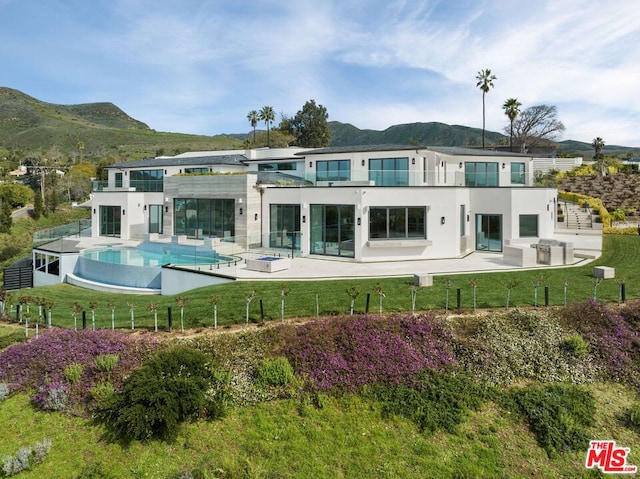 rear view of property with a balcony, a yard, a mountain view, and a patio area