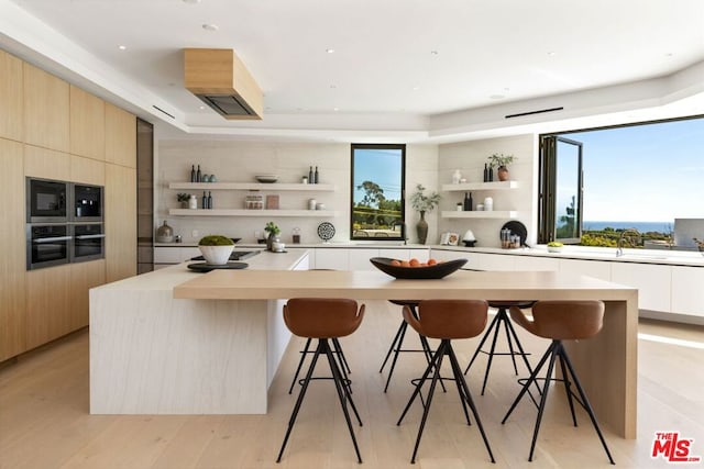 kitchen featuring light brown cabinets, oven, a kitchen breakfast bar, a center island, and light wood-type flooring