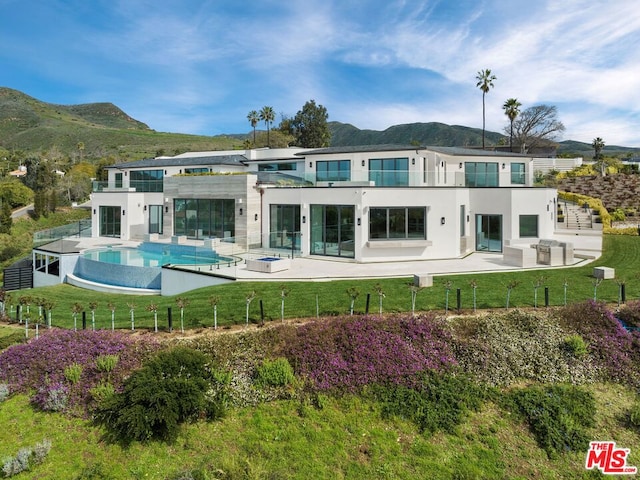 back of property with a lawn, a balcony, a mountain view, and a patio area