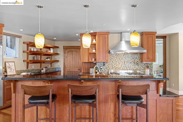 kitchen featuring wall chimney range hood, decorative light fixtures, light hardwood / wood-style flooring, and a breakfast bar