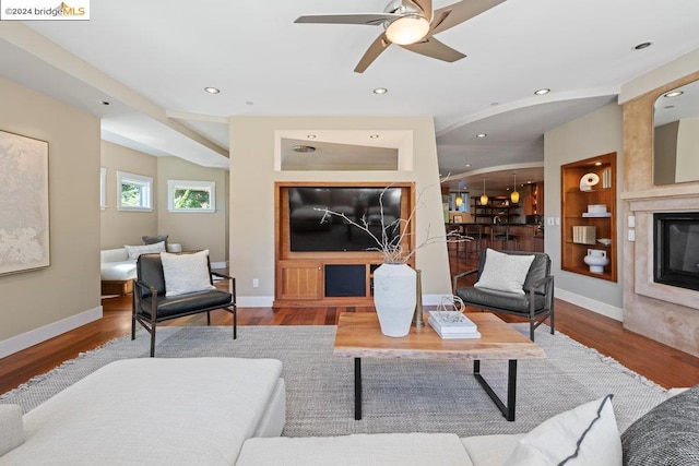 living room with a fireplace, wood-type flooring, built in features, and ceiling fan