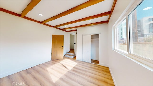 unfurnished bedroom featuring light hardwood / wood-style floors, beamed ceiling, and a closet