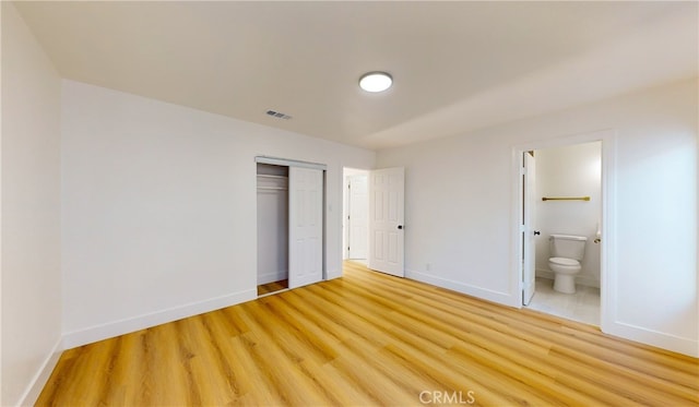 unfurnished bedroom with a closet, wood-type flooring, and connected bathroom