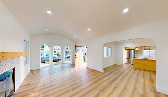 unfurnished living room with light hardwood / wood-style floors, a healthy amount of sunlight, and lofted ceiling