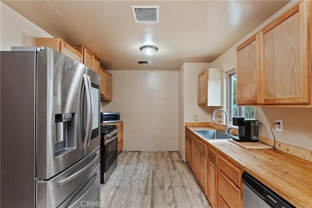 kitchen with stainless steel appliances, wooden counters, light wood-type flooring, light brown cabinetry, and sink