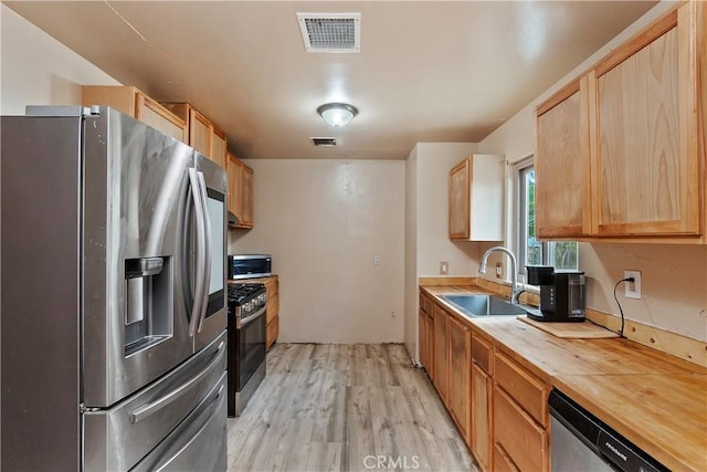kitchen featuring visible vents, a sink, butcher block countertops, light wood-style flooring, and appliances with stainless steel finishes