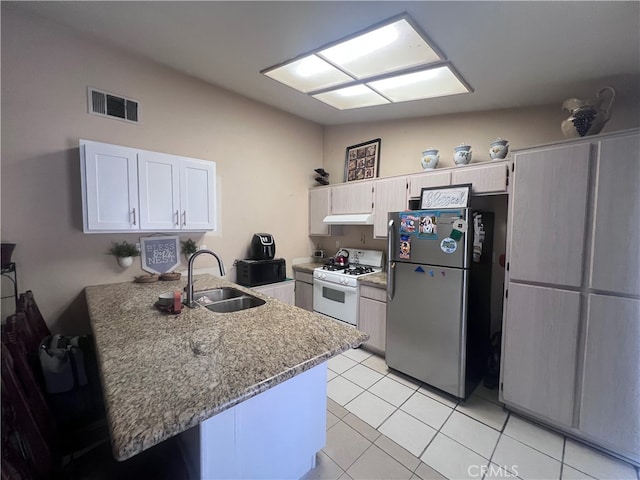 kitchen featuring kitchen peninsula, white gas range oven, sink, and stainless steel refrigerator