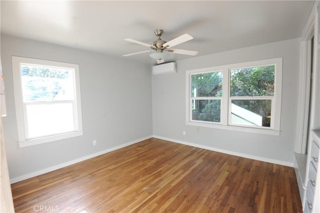 unfurnished room with an AC wall unit, wood-type flooring, a wealth of natural light, and ceiling fan