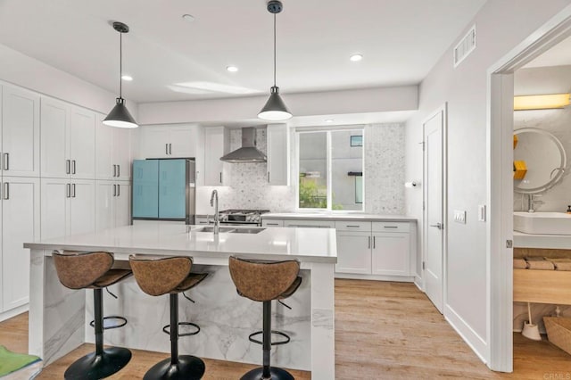 kitchen featuring pendant lighting, light hardwood / wood-style floors, wall chimney exhaust hood, and sink