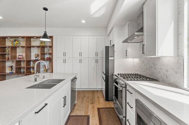 kitchen with light wood-type flooring, wall chimney exhaust hood, stainless steel appliances, sink, and white cabinets