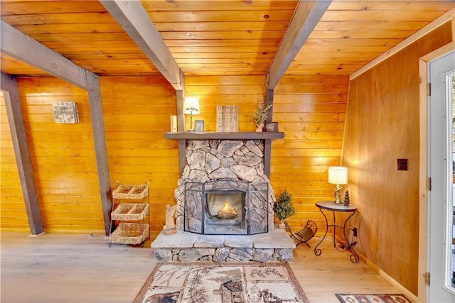 unfurnished room featuring beamed ceiling, wooden walls, a fireplace, and light hardwood / wood-style flooring