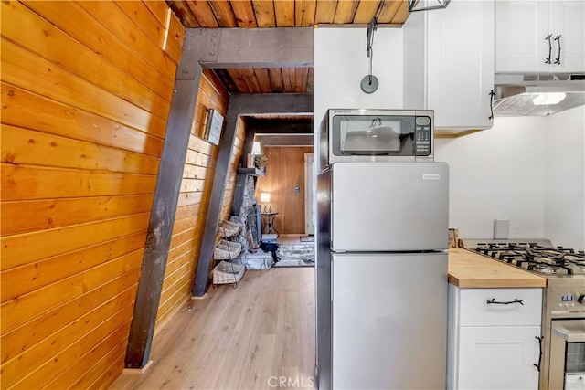 kitchen with white cabinets, appliances with stainless steel finishes, light wood-type flooring, and wood walls