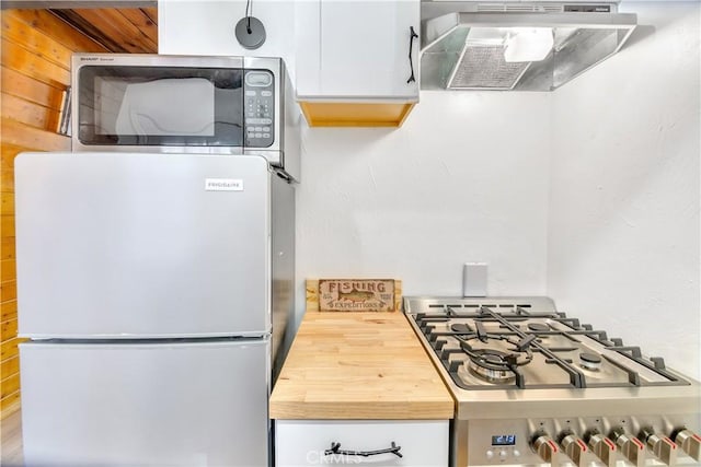 kitchen with extractor fan, wooden walls, stainless steel appliances, and white cabinets