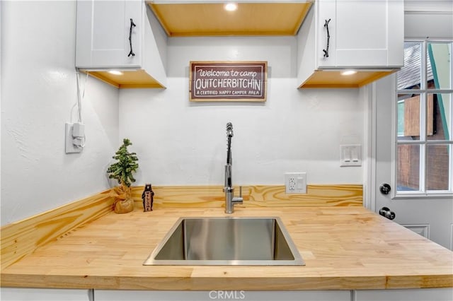 kitchen with white cabinetry, sink, and wood counters