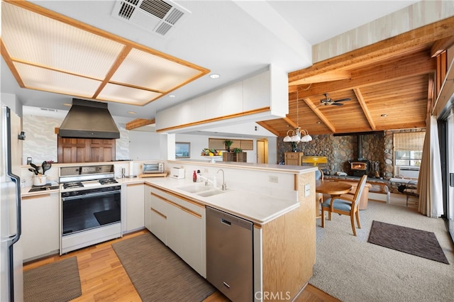 kitchen with kitchen peninsula, sink, a wood stove, stainless steel appliances, and wall chimney exhaust hood