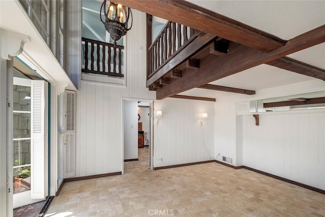 stairway featuring beam ceiling, wood walls, and a chandelier