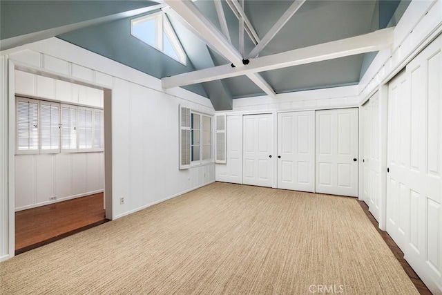 unfurnished bedroom featuring carpet flooring, lofted ceiling with beams, and two closets