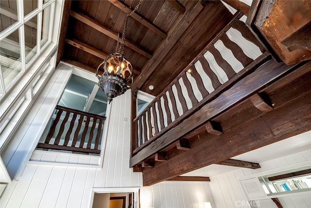 staircase with wooden walls, beamed ceiling, and an inviting chandelier