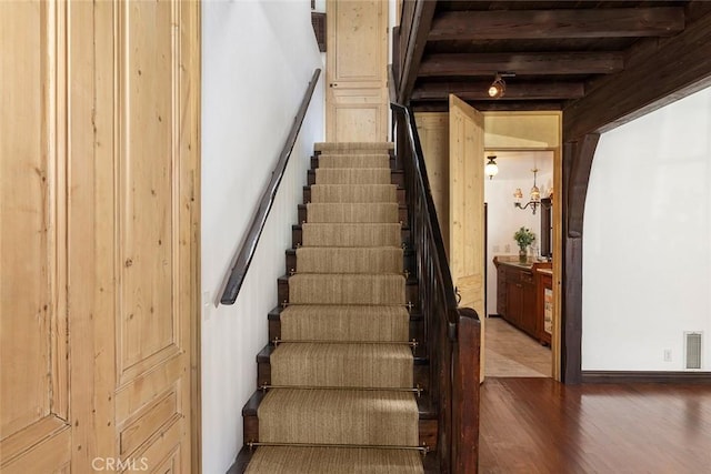 stairs featuring beamed ceiling and hardwood / wood-style flooring