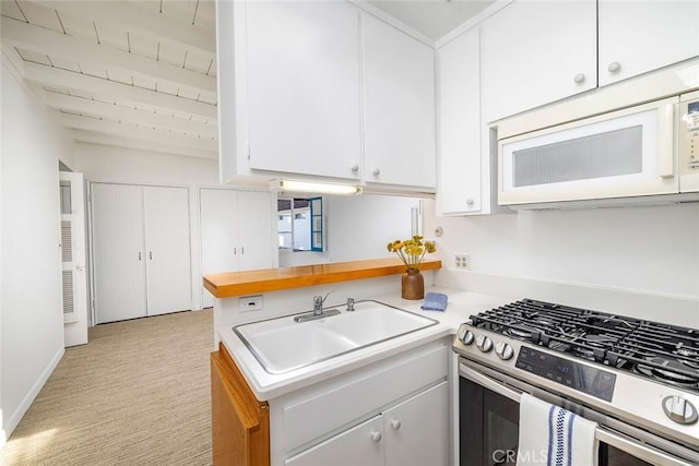 kitchen with stainless steel gas stove, beam ceiling, white cabinetry, and sink