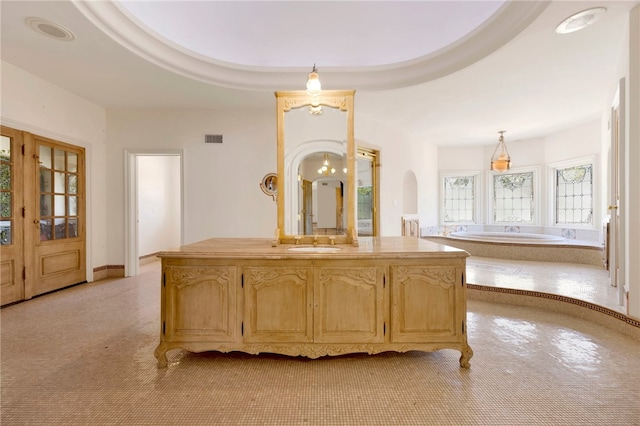 bedroom with a raised ceiling, a bathing tub, and vanity