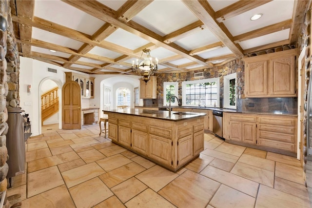 kitchen with a healthy amount of sunlight, stainless steel dishwasher, a kitchen island with sink, and an inviting chandelier