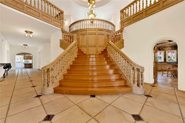 stairs with a notable chandelier, tile patterned flooring, a high ceiling, and a wealth of natural light