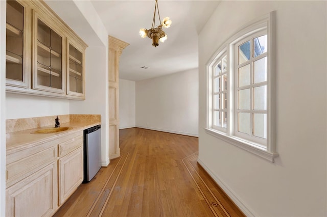 kitchen with light wood-type flooring, a chandelier, sink, hanging light fixtures, and stainless steel dishwasher