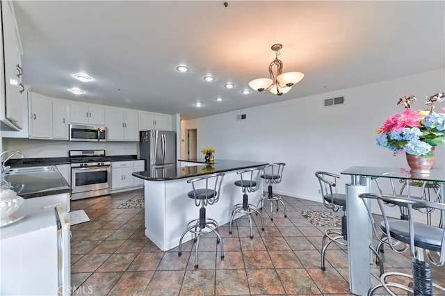 kitchen featuring appliances with stainless steel finishes, decorative light fixtures, white cabinetry, sink, and a breakfast bar