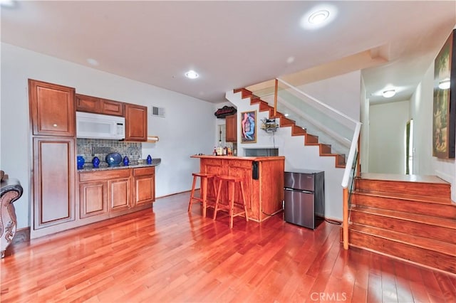 kitchen featuring wood-type flooring, decorative backsplash, a kitchen bar, and stainless steel fridge