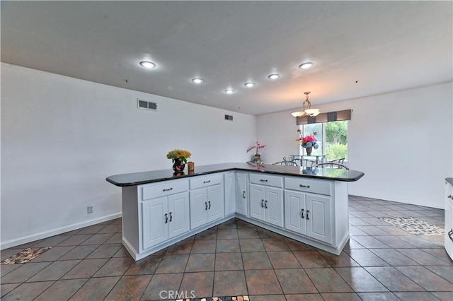 kitchen with kitchen peninsula, dark tile patterned flooring, white cabinetry, and pendant lighting