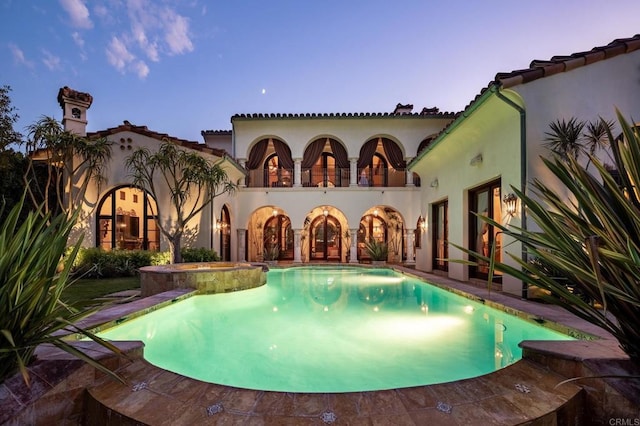 pool at dusk with an in ground hot tub