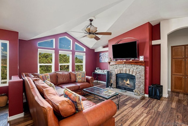 living room featuring ceiling fan, a stone fireplace, dark hardwood / wood-style floors, and vaulted ceiling