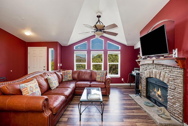 living room featuring vaulted ceiling, ceiling fan, dark hardwood / wood-style floors, and a stone fireplace