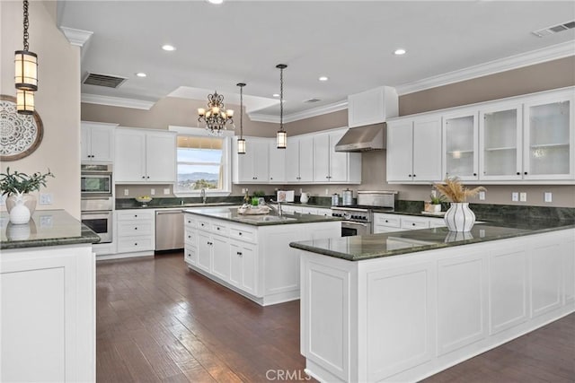 kitchen featuring visible vents, stainless steel appliances, crown molding, wall chimney range hood, and a chandelier