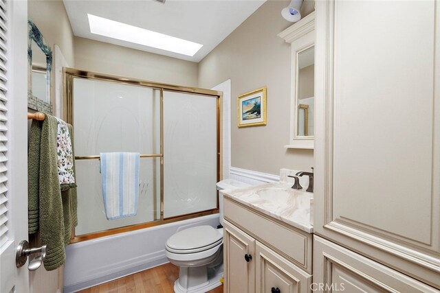 full bathroom featuring vanity, hardwood / wood-style floors, a skylight, bath / shower combo with glass door, and toilet