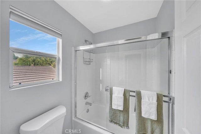 bathroom featuring toilet and shower / bath combination with glass door