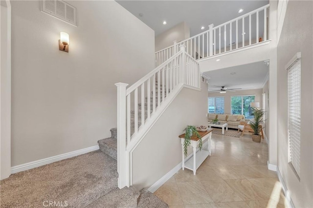 stairs with carpet, ceiling fan, and a towering ceiling